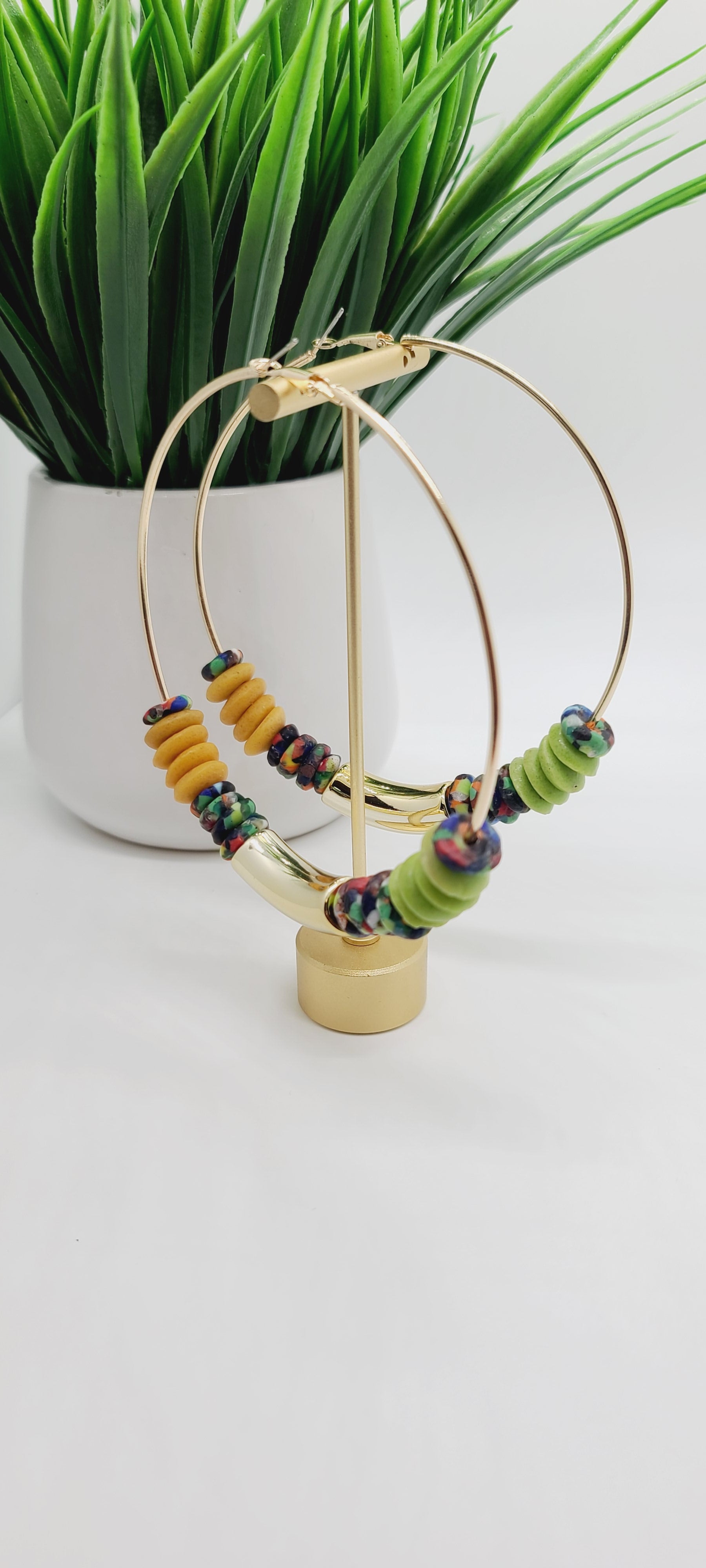 Length: 4x4 inches | Weight: 1.9 ounces  Distinctly You! These earrings are made with large gold Hoops, gold, green, multi-colored print Ashanti glass saucers, and curved gold resin charm.