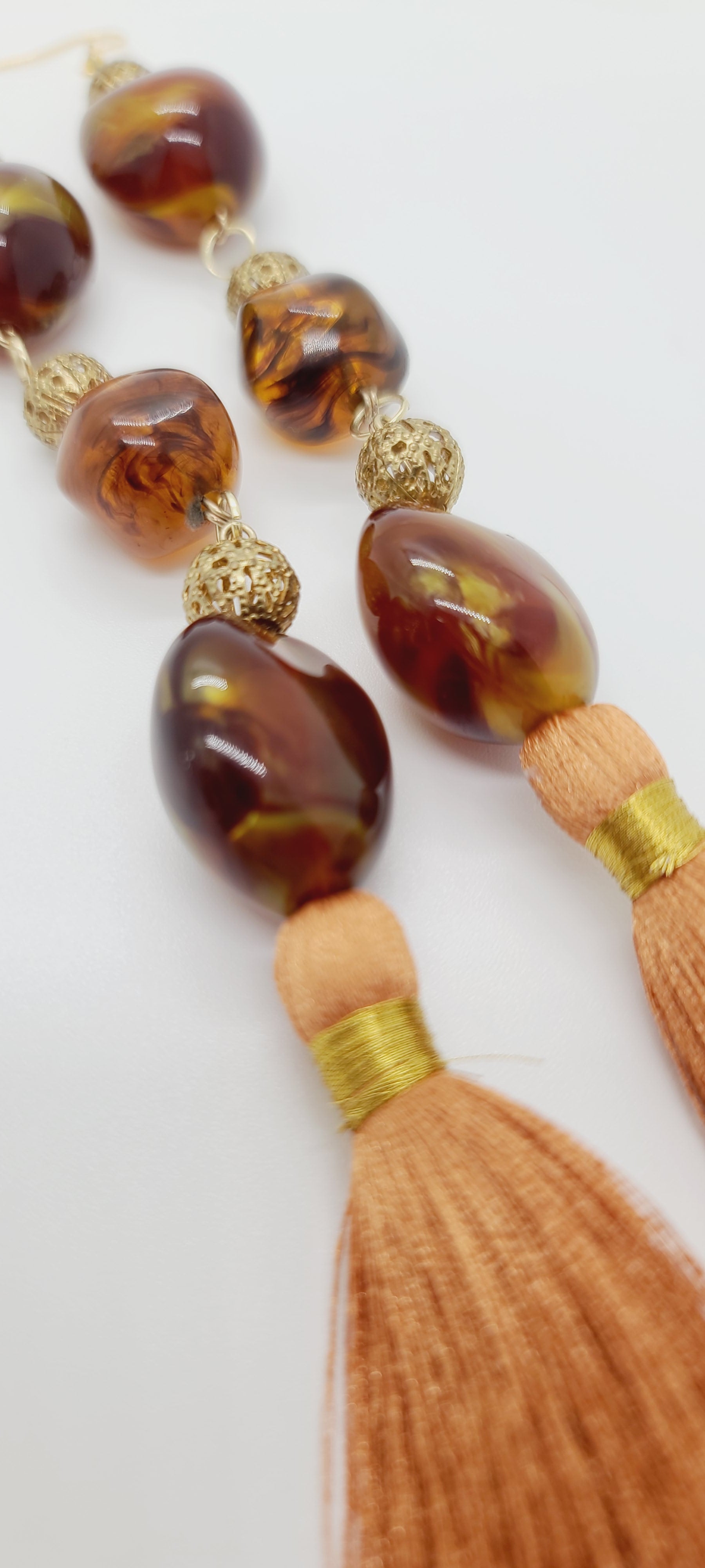 Length: 8.5 inches | Weight: 1.3 ounces  Distinctly You! These earrings are made with orange tassels, amber Multi swirl resin beads, 8mm gold filigree metal bead accents.