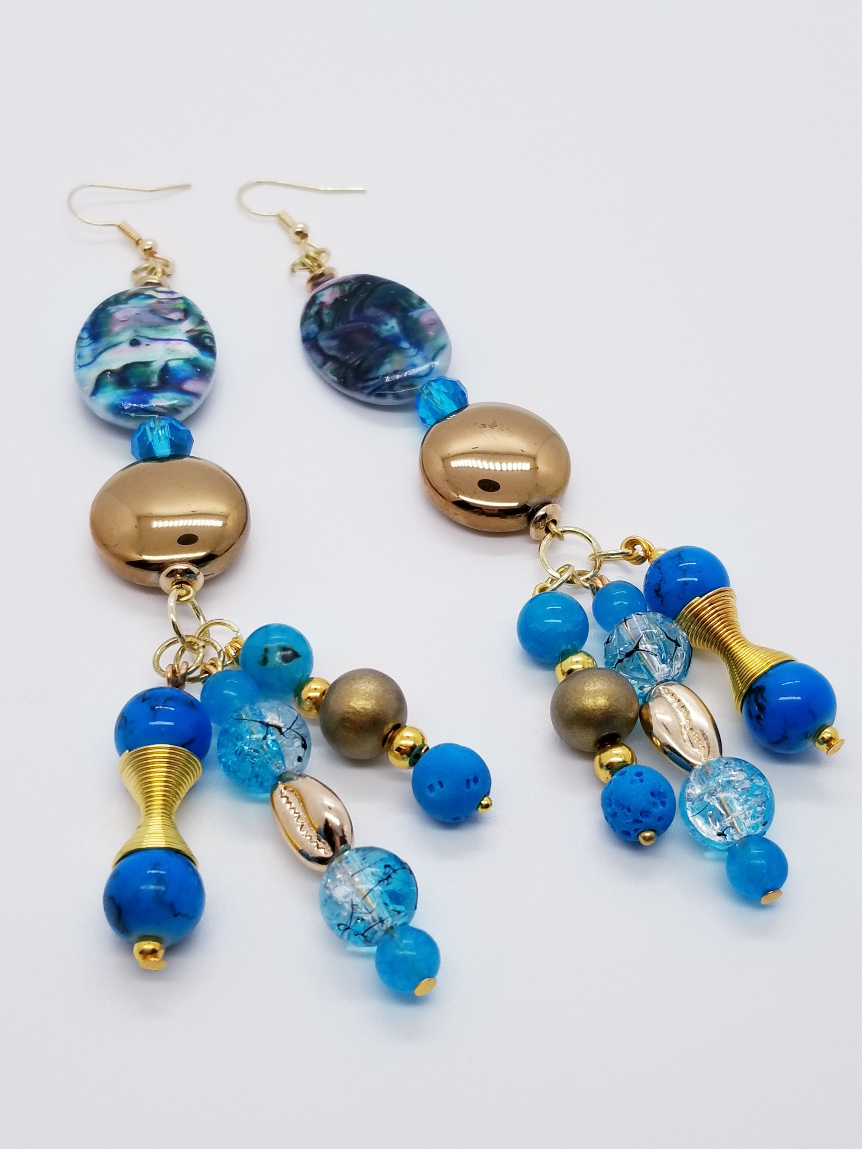 PLEASE BE AWARE: Earrings Hang Past Shoulders   Length: 5.5 inches | Weight: 1.3 ounces  Distinctly You! The earrings are handmade using aqua ceramic swirl oval beads, gold glass discs, 10mm gold wood beads, 10mm blue Czech glass beads, 6mm blue glass beads, gold head pins, and hypoallergenic hooks with back closures. 